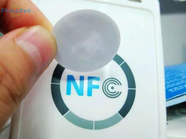Fingers holding a round gray NFC sticker over a white desktop NFC reader