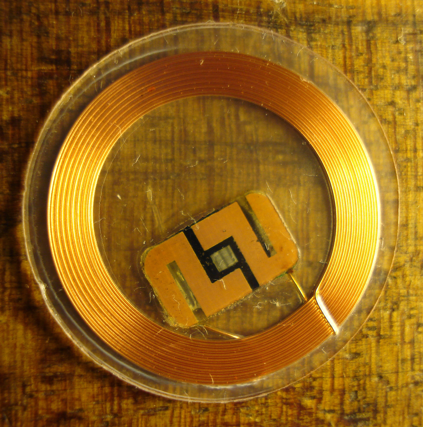 Round clear RFID tag with copper coil antenna and chip on a wooden surface